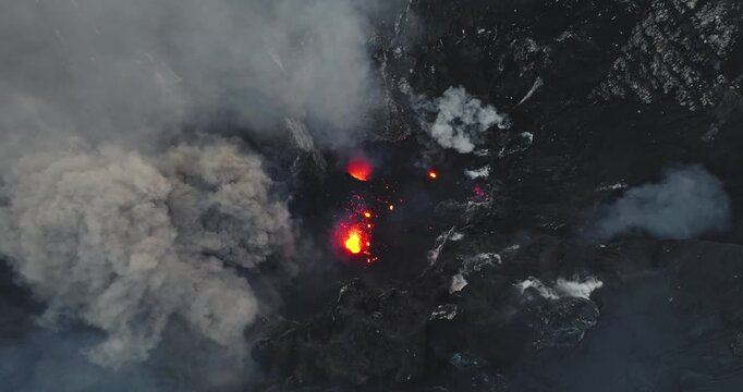 Mount Yasur on Tanna Island is erupting in a dramatic scene, plumes of smoke and ash and red hot lava bursting from multiple vents across the caldera, raw geological power. Aerial drone flight footage