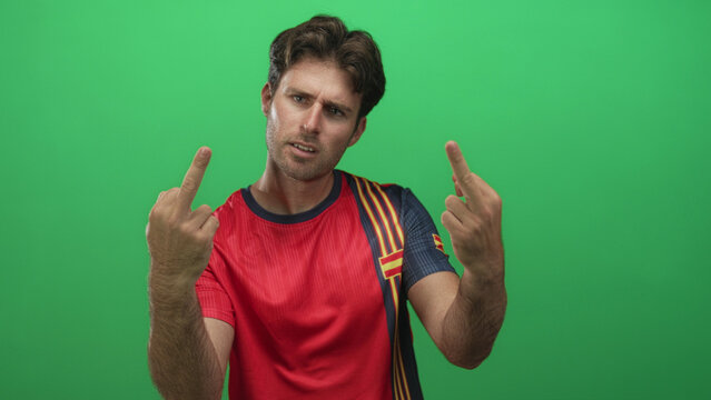 Young hispanic soccer fan man in red jersey shows middle fingers to camera in a green studio setting; defiance protest. - Powered by Adobe