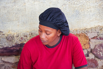 village african woman portrait, satin hair cap bonnet , outdoors in the nature, at home ,wall behind