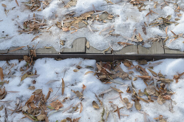 urban landscape featuring wooden deck with frozen snow and ice and dried fallen leaves