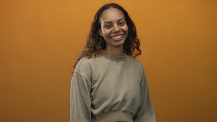 Woman smiling and relaxed wearing a casual cropped sweatshirt in an orange studio portrait; warmth...