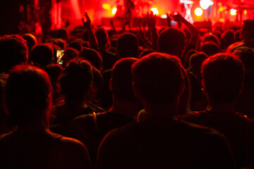 concert crowd in red light, unrecognizable anonymous people cheering at concert in music festival by night