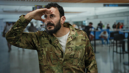 Hispanic man in military uniform saluting in a bustling airport terminal capturing a moment of respect amidst the busy crowd in terminal 1.