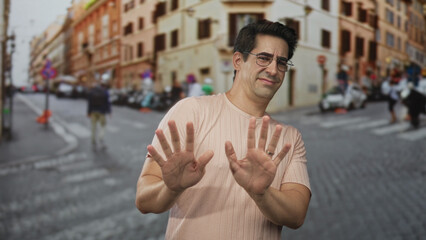 Man pushes palms forward in stop gesture at crosswalk on cobblestone street; hesitation restraint caution.