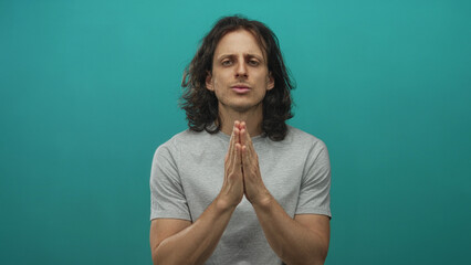 Man with hands pressed together in prayer, palms visible, clasped fingers in studio teal backdrop; hope reflection.