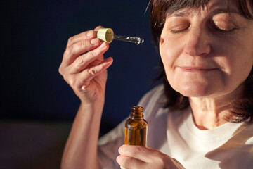 Female Caucasian mature woman applying facial serum with dropper calm skincare ritual wellness...