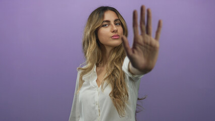 Blonde woman raises hand palm forward in purple studio; denial rejection.