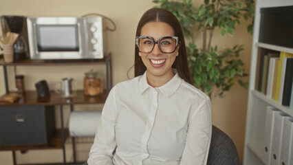 Woman wearing oversized glasses smiling while seated in a building office chair; professional...