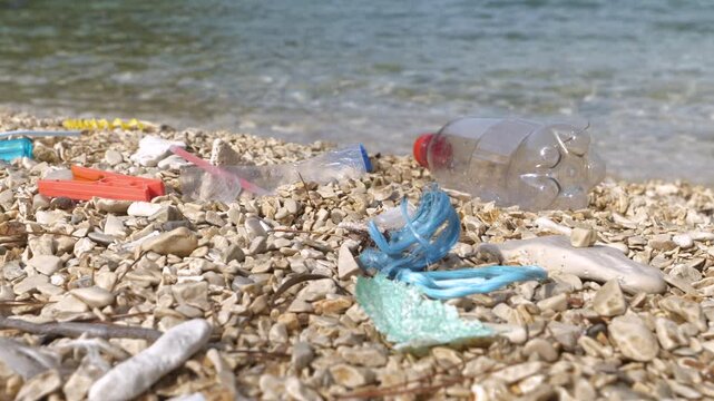 CLOSE UP: Sad sight of plastic garbage remains washed up by sea on pebbly shore. An all too common occurrence on beautiful seaside beaches, which is the result of human carelessness and negligence.