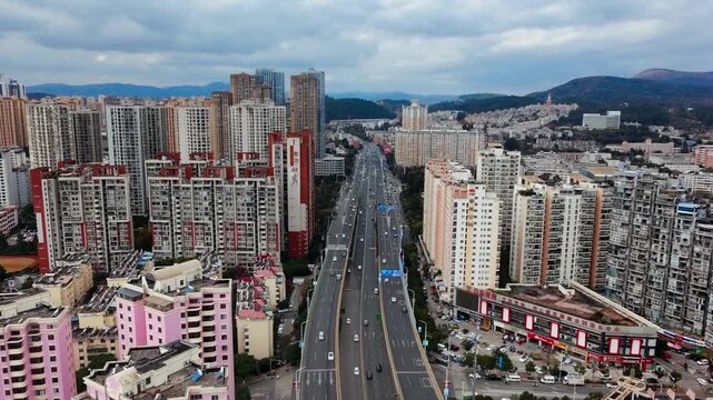 4K Aerial static view of Kunming Second Ring Road traffic, China. Drone shot of double-deck elevated highway, vehicles on viaduct & ground, residential buildings with solar panels under cloudy sky