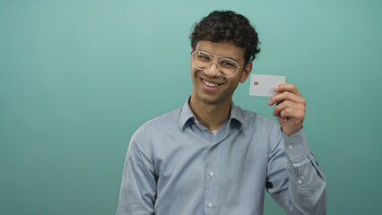 Man holding creditcard with visible chip in studio against green wall while smiling warmly; confidence.