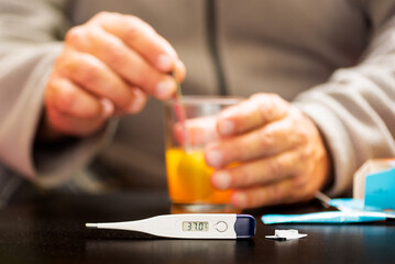 Fever concept with thermometer and person preparing medicine in the background