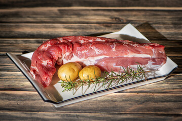 Fresh raw pork tenderloin with potatoes and rosemary on rustic wooden table