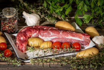 Fresh raw pork tenderloin on a plate with baby potatoes, cherry tomatoes, pepper, garlic and herbs, close up