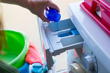 Preparing for a wash cycle of dirty clothes, a hand pours concentrated gel for clean and fresh laundry