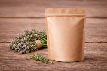 Blank kraft stand-up pouch mockup with thyme herb bouquet on rustic wooden table. Eco-friendly packaging template for organic tea, spices, skincare branding. Minimal copy space for label.