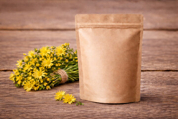 Blank kraft stand-up pouch mockup with zipper on rustic wooden table and yellow wildflowers. Eco packaging template for herbal tea, spices, cosmetics branding, copy space.