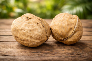 Two whole walnuts in shell on rustic wooden table, close-up with green bokeh background, natural light, copy space. Organic healthy snack, food ingredient concept.