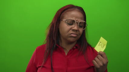 Woman holds a yellow sticky note with tax text in a bright green studio setting wearing a red shirt...