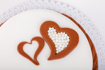 A close-up shot showcases a white cake adorned with two hearts outlined in brown, one filled with...