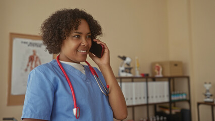 Woman doctor holds smartphone to ear and gestures with hand in clinic building while wearing blue...