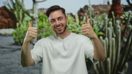 Young man with beard smiling outdoors in park surrounded by nature giving thumbs up showing positivity and happiness