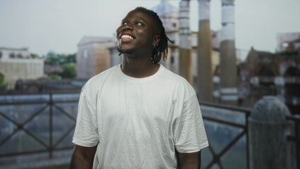 Man smiling with face and teeth visible, wearing white t shirt, standing on old town street in...