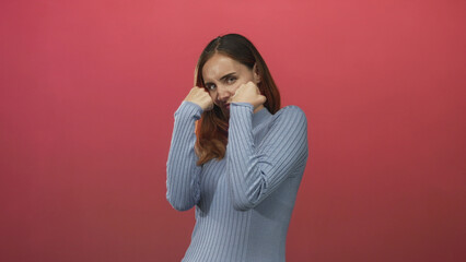 Woman throwing a punch with clenched fist and raised guard in a studio wearing a blue sweater; determination self defense.