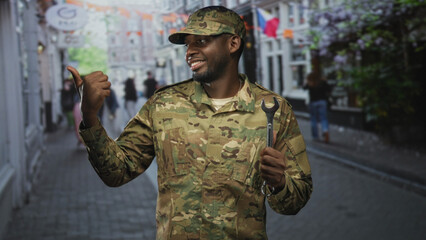 Man soldier in camouflage uniform holds wrench and gives thumbs up while pointing over shoulder on...