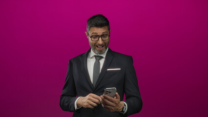 Man in business suit and tie tapping a smartphone with both hands while reading the screen in...