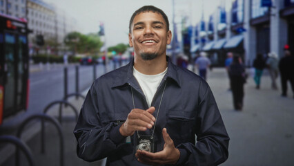 Man with visible badge and id claps hands on a busy city street while smiling, wearing dark jacket...