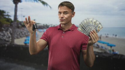 Man holding car keys and a fan of cash, winks while pointing keys toward camera on beach;...