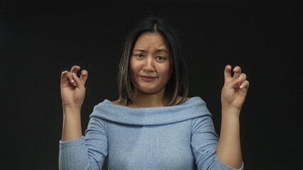 Woman expressing confusion in thoughtful gestures over isolated black background, wearing blue in contemplative mood and unsure expression with hands raised in quote symbol.