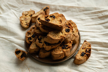 Stack of italian biscotti cantuccini cookies with nuts and raisins on a plate over white linen tablecloth