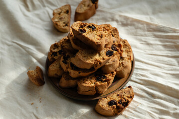 Stack of italian biscotti cantuccini cookies with nuts and raisins on a plate over white linen tablecloth