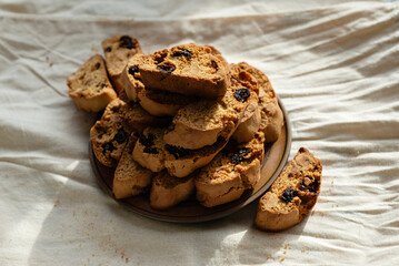Stack of italian biscotti cantuccini cookies with nuts and raisins on a plate over white linen tablecloth