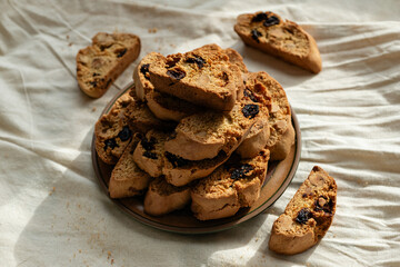 Stack of italian biscotti cantuccini cookies with nuts and raisins on a plate over white linen tablecloth
