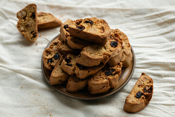 Stack of italian biscotti cantuccini cookies with nuts and raisins on a plate over white linen tablecloth