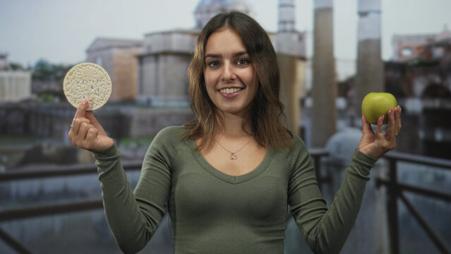 Woman smiling holding green apple and rice cake with hands in front of building; mindful eating wellness joy.