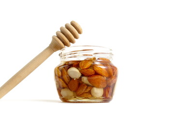 On a white background there is a glass jar filled with honey and nuts.	
