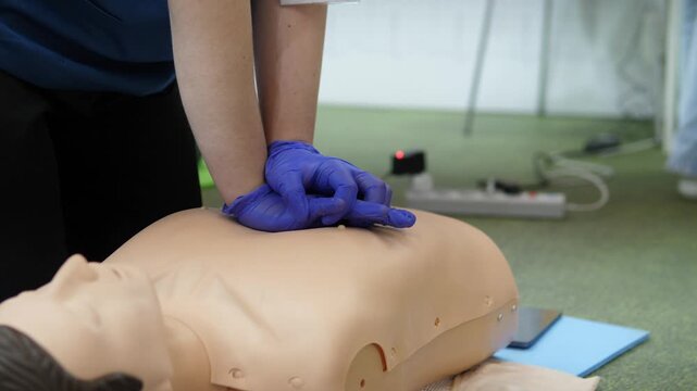 focused handsonly chest compressions on training mannequin with gloved instructor workplace safety course captures correct posture and compression rhythm, clipboard and feedback device