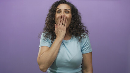 Hispanic woman with hand covering mouth and playful expression in purple studio setting wearing...