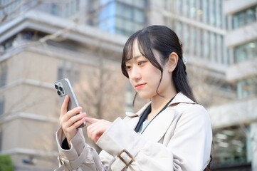 ビル街でスマホを使用する日本人ビジネスウーマン