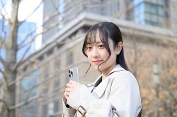 ビル街でスマホを使用する日本人ビジネスウーマン