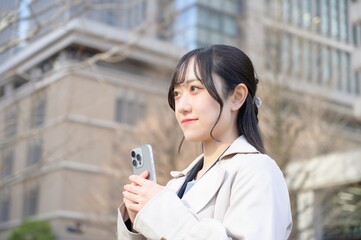 ビル街でスマホを使用する日本人ビジネスウーマン