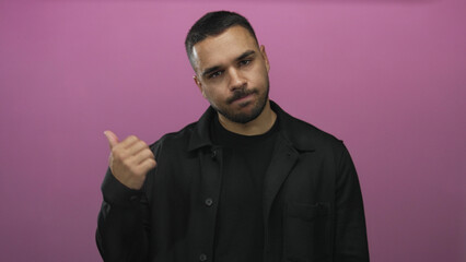 Obraz premium Young hispanic man wearing black shirt with neutral expression showing thumb up gesture in a pink studio setting; confidence.