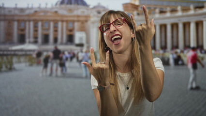 Obraz premium Woman making rock horns with hands in vatican square, red glasses and watch visible; playful defiance.