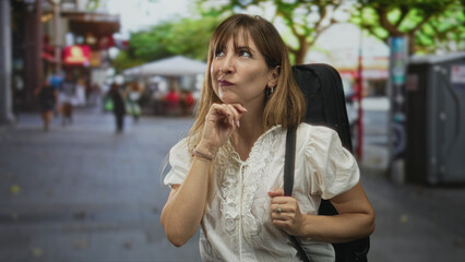 Fototapeta premium Woman points finger upward on busy city street while carrying a guitar case and wearing a white blouse; playful curiosity.