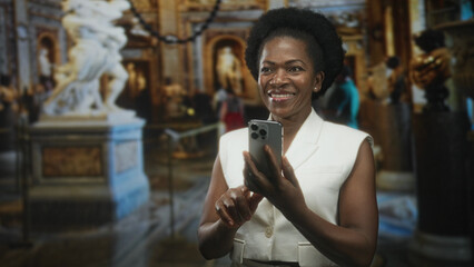 Woman holding smartphone tapping screen with finger while smiling among classical sculptures in an...