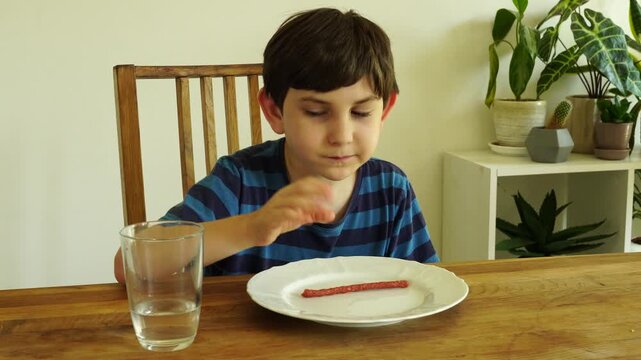Boy eats dried cabanossi at the table
